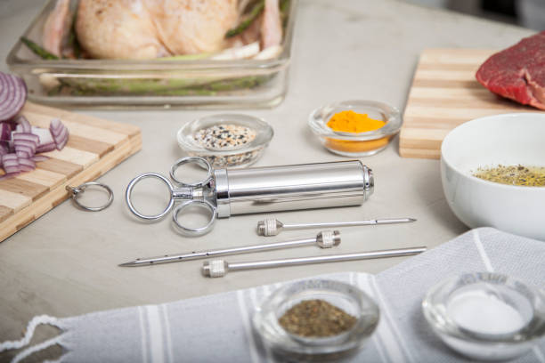 Stainless Steel meat injector being used in kitchen with raw check and steak meat stock photo