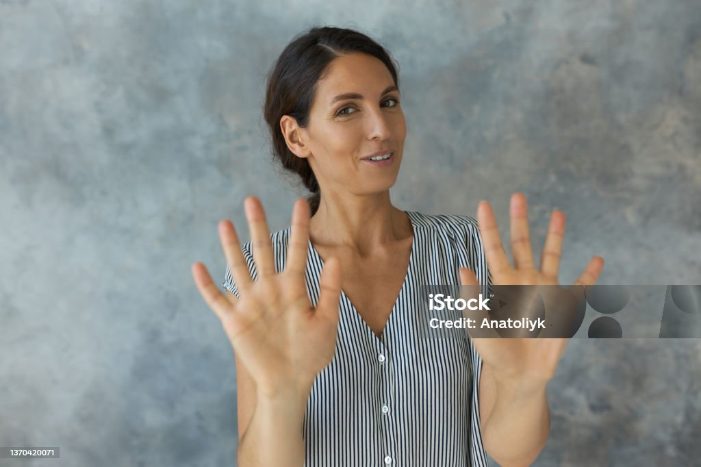 Studio shot of attractive young Caucasian woman showing "no-no-no" gesture, refusing from offer, food or drinks, or giving "please don"u2019t touch me" sign, smiling. Body language. Personal boundaries Cheerful Stock Photo