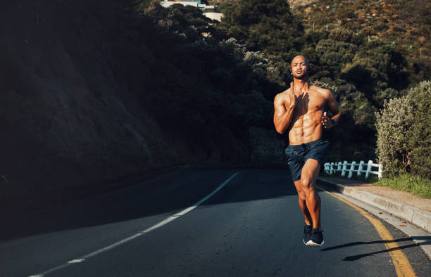 colpo di un giovane sportivo che corre all'aperto - men beach running shirtless foto e immagini stock