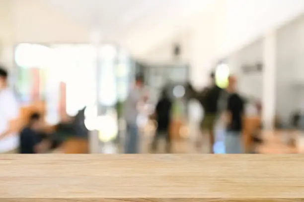 Photo of Empty wooden table with blurred businesspeople in meeting room. Copy space for display of product.