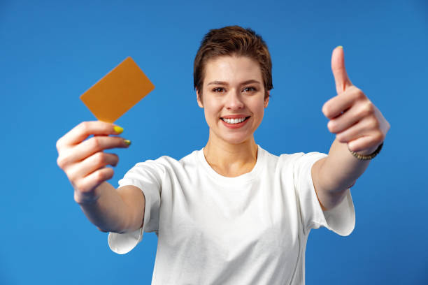 imagen de una mujer joven sosteniendo una tarjeta de visita con espacio de copia sobre fondo azul - invitation blank smiling business card fotografías e imágenes de stock
