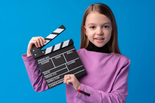 istock Smiling girl holding clapper board against blue background 1370427510