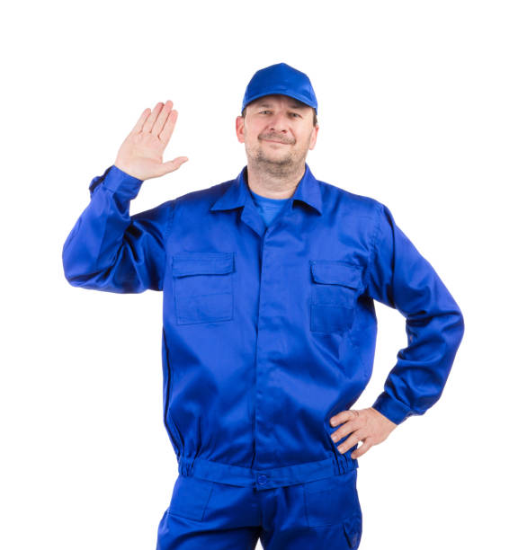 istock A man in work clothes stands with his hand raised in greeting. 1370431041