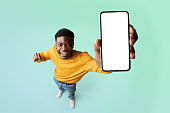 Excited black guy demonstrating smartphone with blank white screen, showing free copy space for your ad, mockup