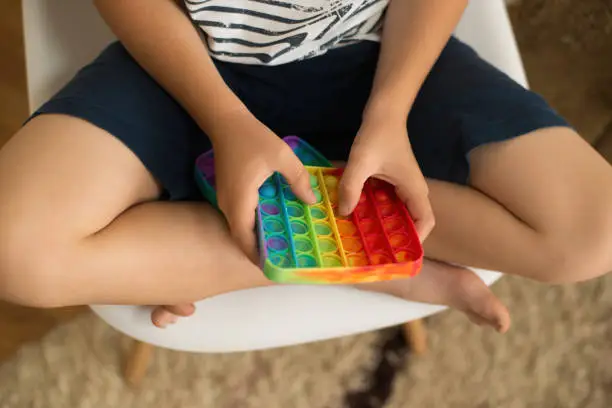 Photo of popular colorful anti-stress touch toy fidget push pop it in the hands of a child, popit toy