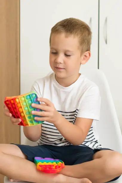 Photo of popular colorful anti-stress touch toy fidget push pop it in the hands of a child, popit toy