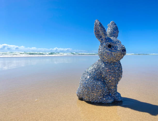 istock Silver sparkly glitter Easter Bunny at the beach.  Sitting on the sand at the waters edge. Blue ocean and sky in the background. Gold Coast Queensland Australia 1370435793