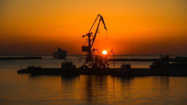 istock Backlit cranes and ship in the port at sunrise with fire sky 1370436076