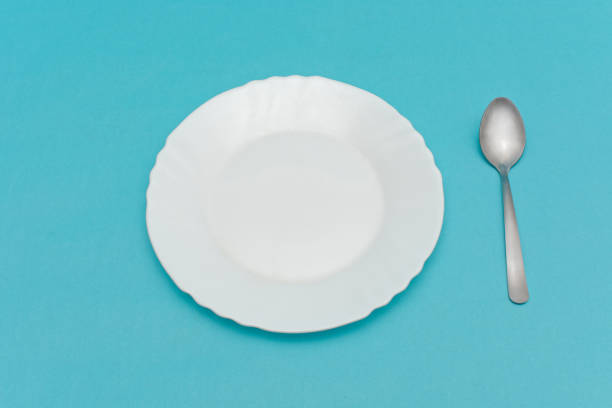 istock White plate and spoon isolated on blue background. 1370436178