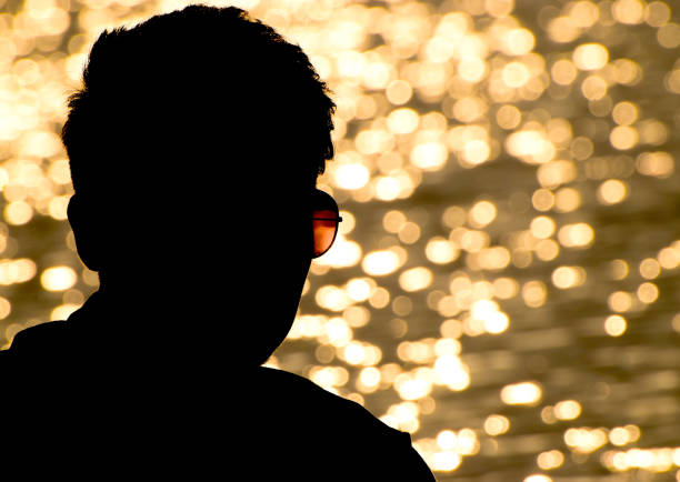 A young man standing by the lakeside during twilight. The serene atmosphere is enhanced by the soft light reflecting off the tranquil water and the subtle hues of the twilight sky. A young man by the lakeside during twilight