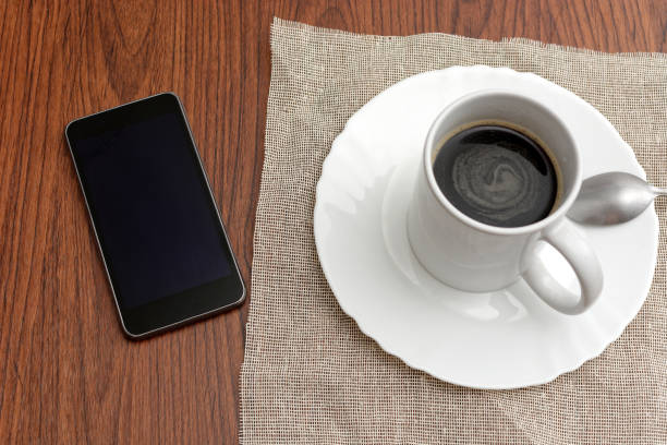 istock Cup of coffee and cell phone on wooden table. 1370437083
