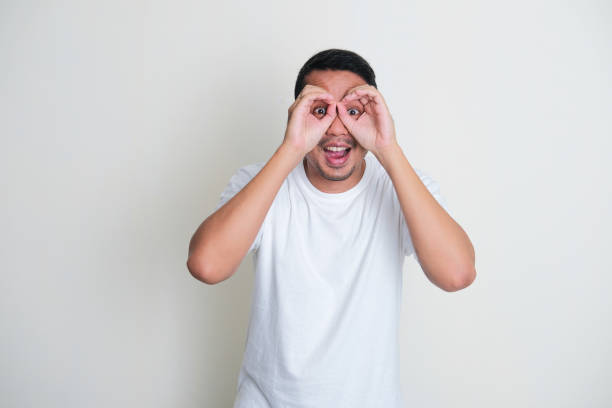 istock Adult Asian man making binoculars shape with his hands and looking through it with excited expression 1370442589