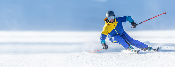 A young aggressive skier on an alpine slope demonstrates an extreme carving skiing style. He is skiing on morning perfectly groomed piste.
