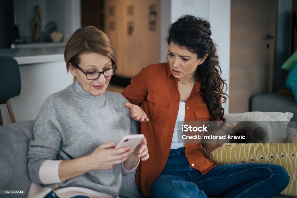 Young woman is arguing with her mother Young woman is arguing with her mother. They are sitting on sofa with legs crossed and senior woman is using smart phone and wearing eyeglasses.. Mother Stock Photo