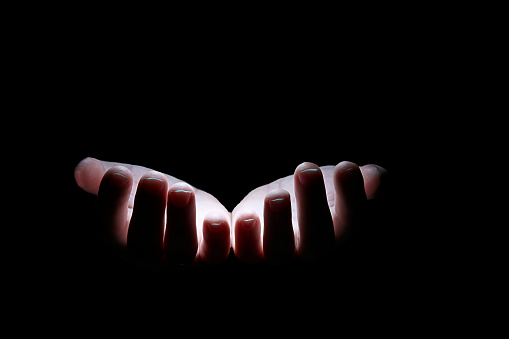 Two palms of a person in the dark are illuminated by light. Two human hands on a black background in white light. Close-up of the isolate.