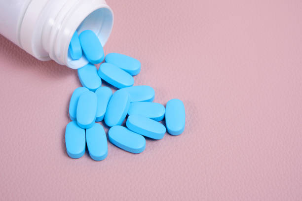 Scattering blue pills from bottle on pink background top view