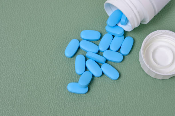 istock Scattering blue pills from bottle on green background top view. 1370448299