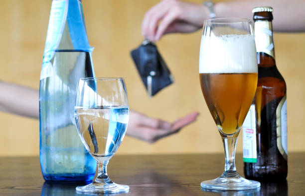 Don’t drink and drive: Bottles and glasses with beer and water in the foreground, a drunken beer drinker gives his car key away to another people in the blurred background - selective focus Bottles and glasses with beer and water on a table in the foreground, the hand of a drunken beer drinker gives his car key away to another people in the blurred background - selective focus dont drink this water stock pictures, royalty-free photos & images