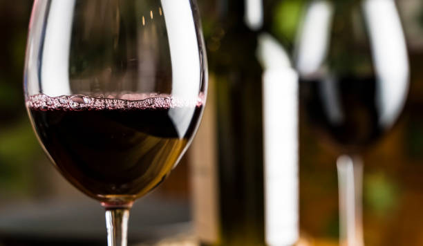 weinprobe. ein glas rotwein auf dem hintergrund eines restauranttisches mit flasche bei einem abendessen oder einer eventparty. - wine bottle bottle burgundy wine stock-fotos und bilder