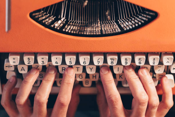 Close-up of hands working on orange vintage typewriter. Literary writer Close-up of hands working on orange vintage typewriter. Literary writer typewriter keyboard communication text office stock pictures, royalty-free photos & images