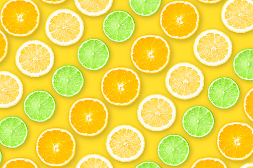 Stock photo showing citrus fruit slices on white background, modern minimalist photo of circular sliced pink grapefruit, oranges, lemon and lime citrus fruits showing segments, seeds / pips and rind around edge with leaves, healthy eating poster wallpaper background design.