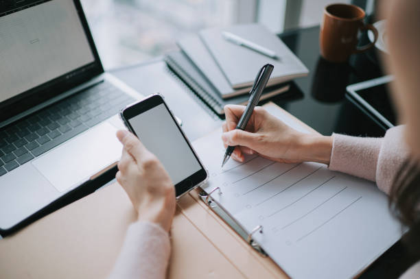 istock Asian Chinese woman writing and using smart phone studying working at home 1370457185