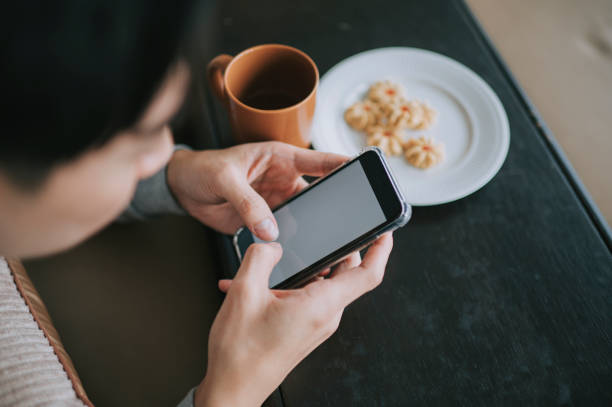 istock Asian Chinese man using smart phone in living room sitting on sofa relaxing during weekend afternoon 1370457186