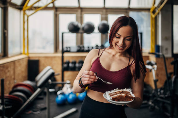 One woman, portrait of a young woman standing in gym alone, she is holding a plate with a slice of cake.