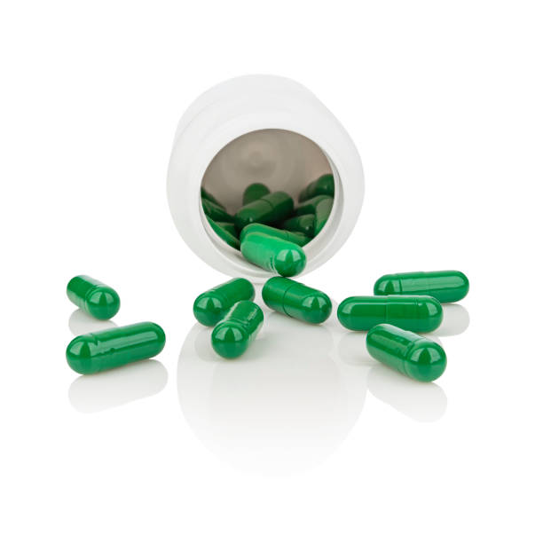 Green medicine capsules pouring from a box Green medicine capsules pouring from a pill bottle. isolated on white background with reflections vitamin photos stock pictures, royalty-free photos & images