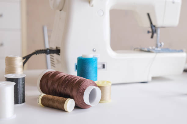 Spools of multi-colored thread and scissors on the table next to the electric sewing machine. Accessories for tailoring.