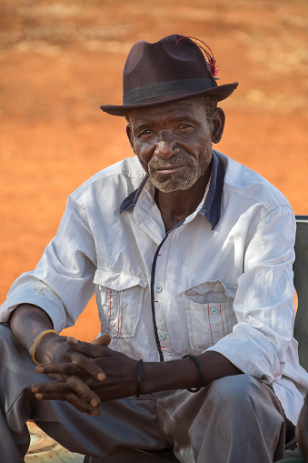 Old African man with a hat siting on a chair in his yard
