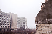 A broken brick wall in close-up against the ruins of a building and a gray sky in the fog. Background