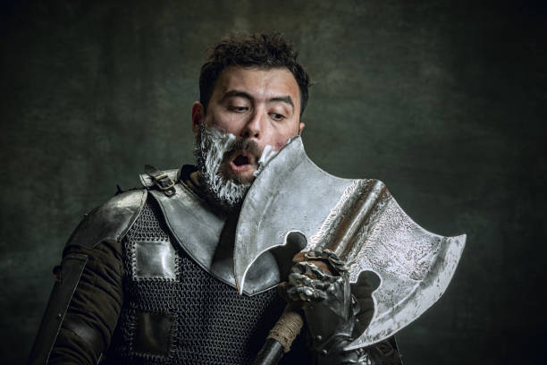 retrato cômico de guerreiro medieval ou cavaleiro com rosto ferido sujo raspando com um machado isolado sobre fundo vintage escuro. comparação de eras, história, beleza - ancient weapon audio - fotografias e filmes do acervo