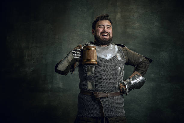 feliz guerrero medieval o caballero con la cara sucia herida sosteniendo una gran taza de cerveza aislada sobre un fondo vintage oscuro. comparación de épocas, historia - chainmail fotografías e imágenes de stock