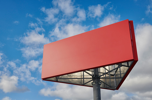 Red billboard in triangle shape and blue sky with fluffy clouds.