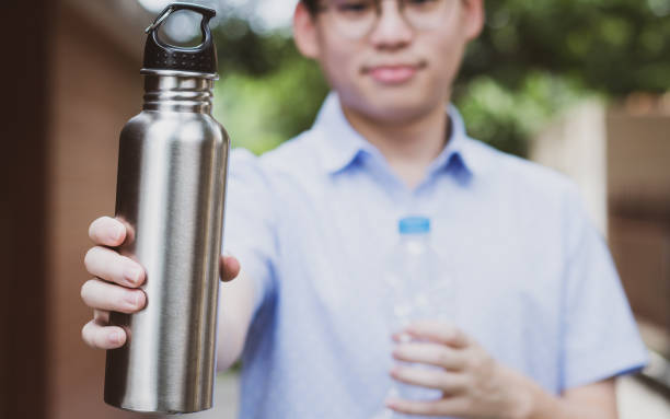 istock Handsome Asian man smiling with confidence holding and showing reusable stainless water bottle and single use plastic bottle in comparison. 1370475064