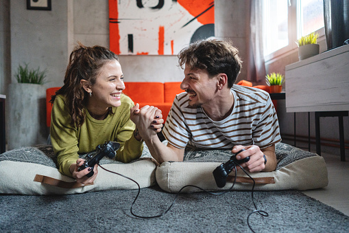 Modern young Caucasian couple lying on the floor while playing video games