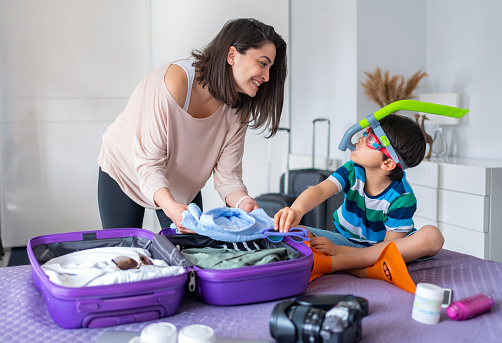 Mother And Son Preparing Travel Suitcase On Bed At Home