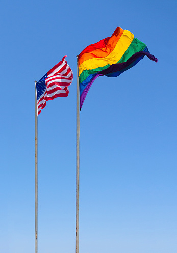 US and LGBT flags are fluttering in the wind against the blue sky