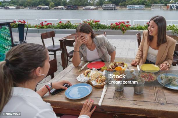 Embarrassed Young Woman Laughing With Friends In Outdoor Restaurant Serving Mexican Snacks Stock Photo - Download Image Now