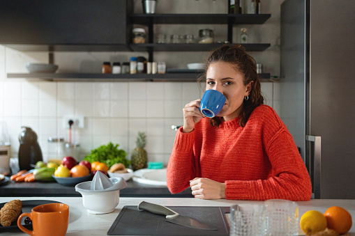 Portrait of serene young Caucasian woman drinking coffee in her modern kitchen