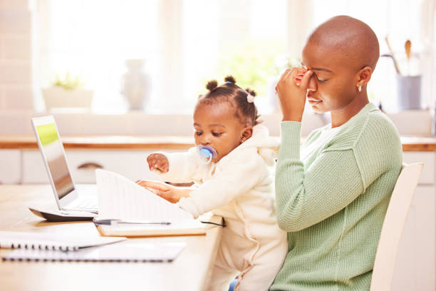 aufnahme einer jungen mutter, die gestresst aussieht, während sie ihr baby hält und von zu hause aus arbeitet - working mother working mother balance stock-fotos und bilder