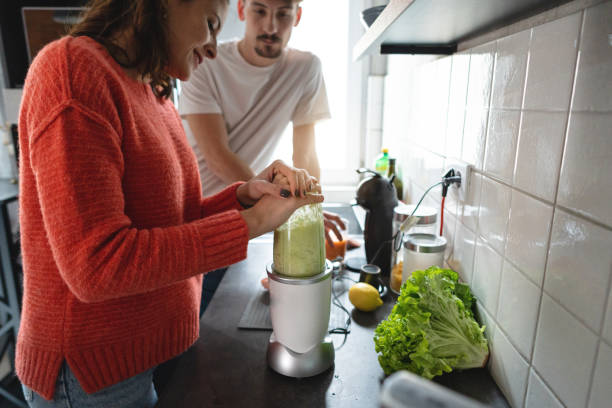istock Young Caucasian couple, in modern kitchen making green smoothie 1370484250
