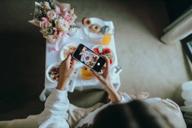 Woman photographing room service breakfast in a hotel room Young woman wearing a bathrobe photographing with a smartphone luxurious room service breakfast in a hotel room room service stock pictures, royalty-free photos & images