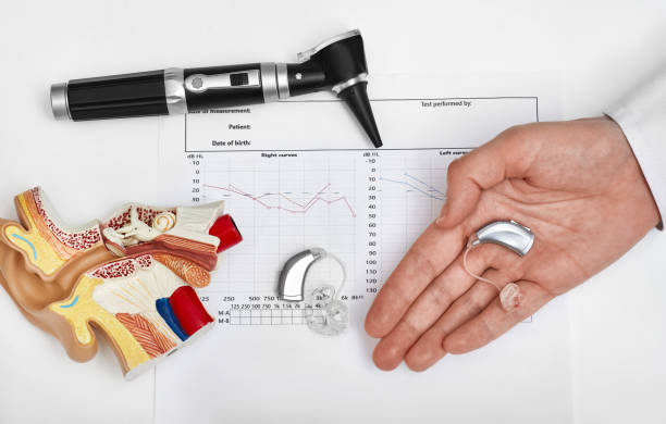 Hearing aid in doctor hand near patient audiogram test , otoscope and anatomical model of human ear, view from above. Hearing and auditory health concept stock photo