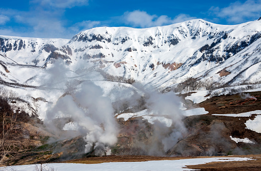Emissions of gas, steam and water from thermal geysers in the valley of Geysers. May snow landscape with a view of the Kamchatka valley of Geysers.