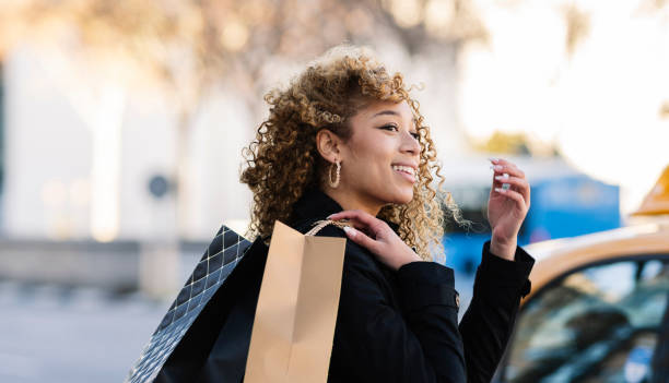 bonita mujer hispana con el pelo rizado caminando con bolsas de compras por la ciudad, - purple belt fotografías e imágenes de stock