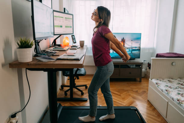 Woman at home office is walking on under desk treadmill Woman working from home at standing desk is walking on under desk treadmill standing desk photos stock pictures, royalty-free photos & images