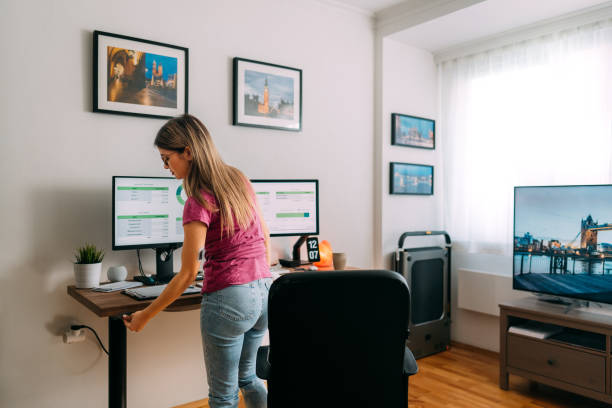 Woman working at standing desk adjusting the height Woman working at home pressing button to adjust the height of standing desk standing desk photos stock pictures, royalty-free photos & images