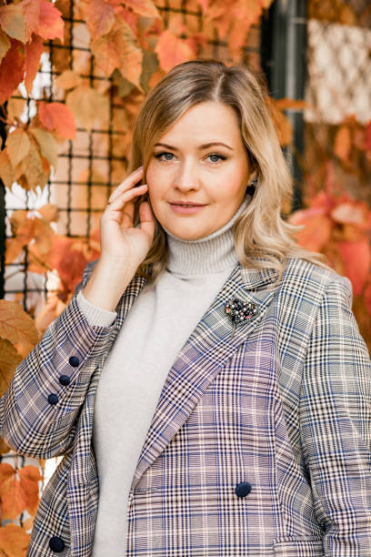 istock Good-looking smiling middle-aged woman in checkered jacket and grey roll-neck sweater pose titivating long blonde hair. 1370489824